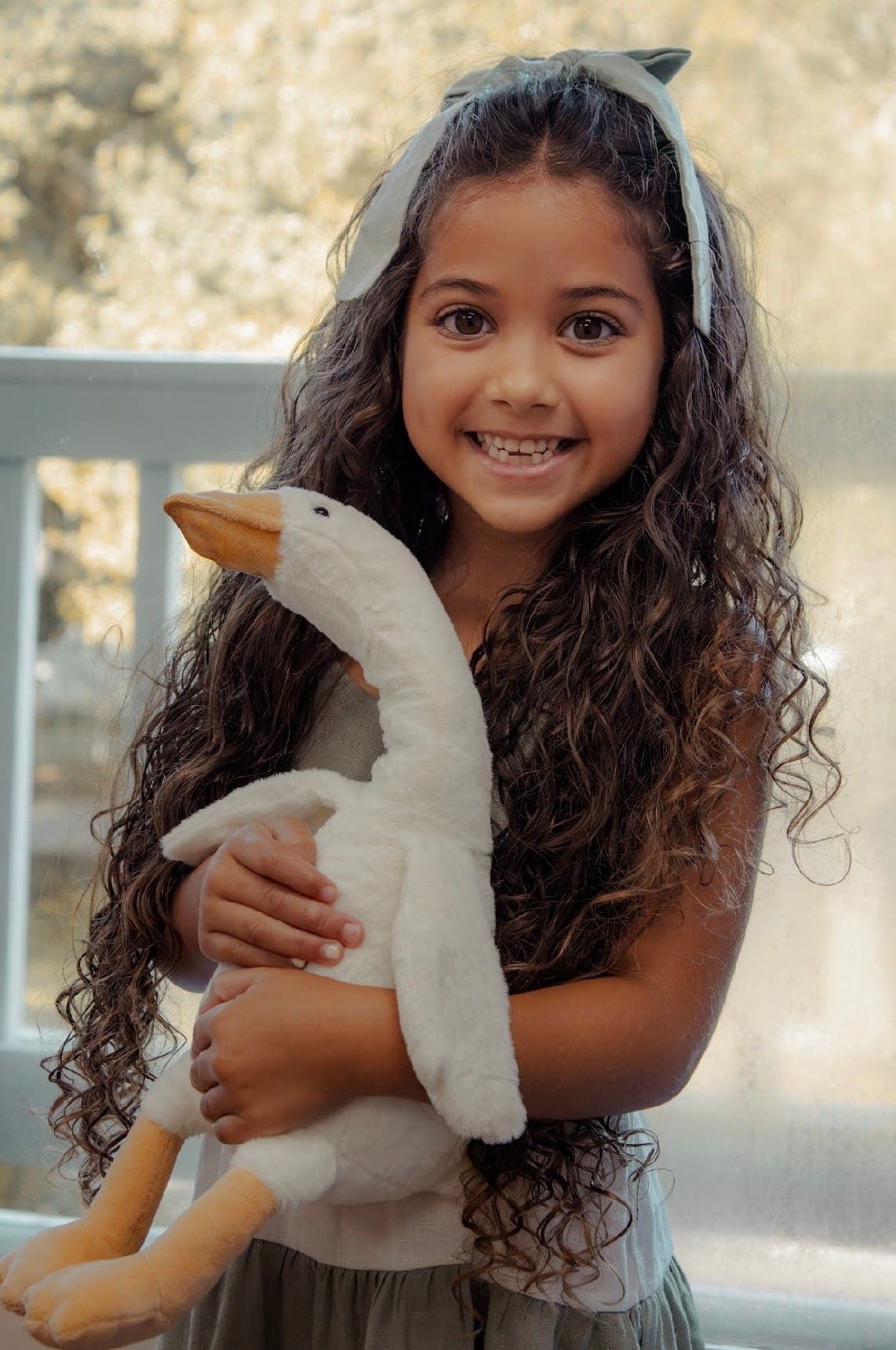 A little girl grinning as she hugs her plush Silly Goose