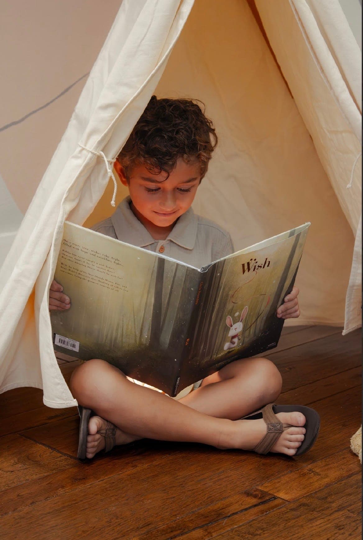 A young reader tucked into a play tent, lost in a picture book during Storytime at Home